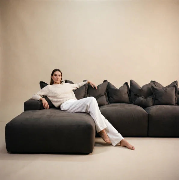 Woman lounging on a modern dark grey sectional sofa with plush cushions in a minimal room