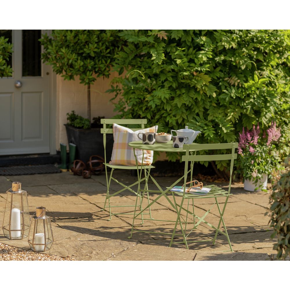 Green metal bistro set with table, two chairs, and cushions on patio, perfect for outdoor dining or garden relaxation.