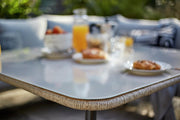 Outdoor dining table with glass top and woven edge, set for breakfast with pastries and juice