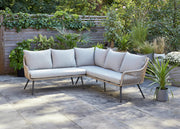 Luxury outdoor corner sofa with light cushions on patio, surrounded by greenery and potted plants