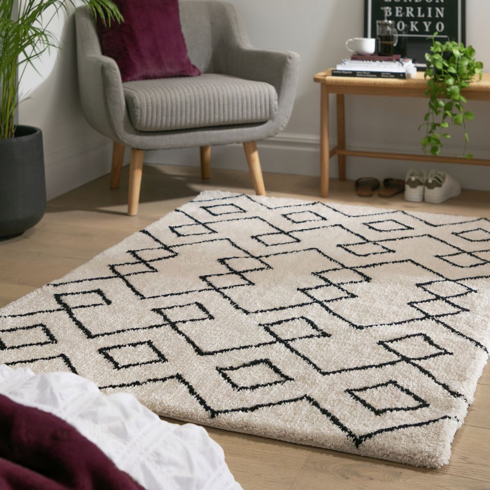 Cream geometric rug with black pattern in modern living room, styled with grey armchair and plants