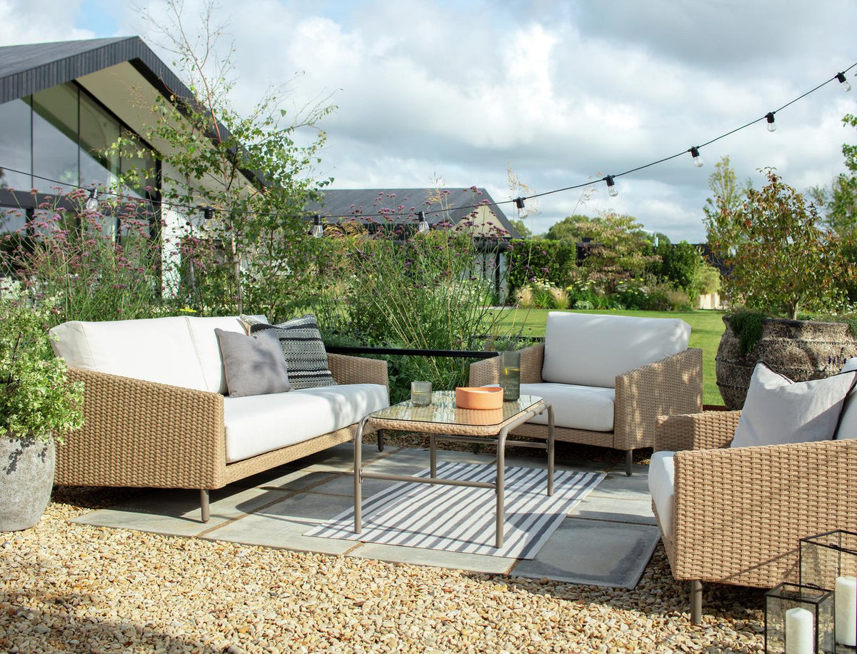 Luxury outdoor wicker sofa set with white cushions, glass table, and string lights in garden patio setting
