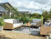 Luxury outdoor wicker sofa set with white cushions, glass table, and string lights in garden patio setting