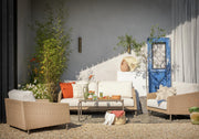 Luxury outdoor wicker sofa set with white cushions, orange throw pillows, and glass coffee table on gravel patio