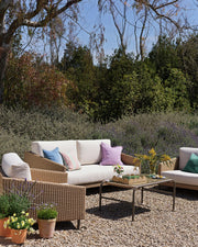 Luxury outdoor wicker sofa set with white cushions and colorful pillows in a garden with lavender and trees