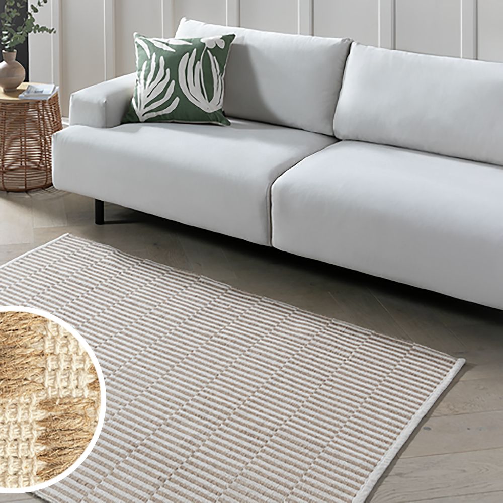 Modern white sofa with green leaf pillow on textured rug in living room