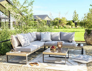 Luxury outdoor sectional sofa with grey cushions, glass coffee table, and patterned rug in a sunny garden setting