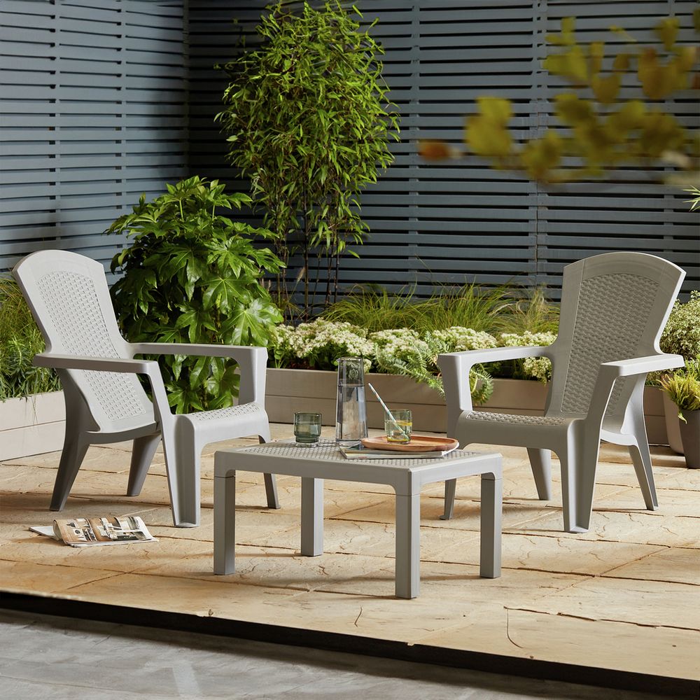 Grey outdoor patio chairs and table set on stone deck with greenery, perfect for garden relaxation