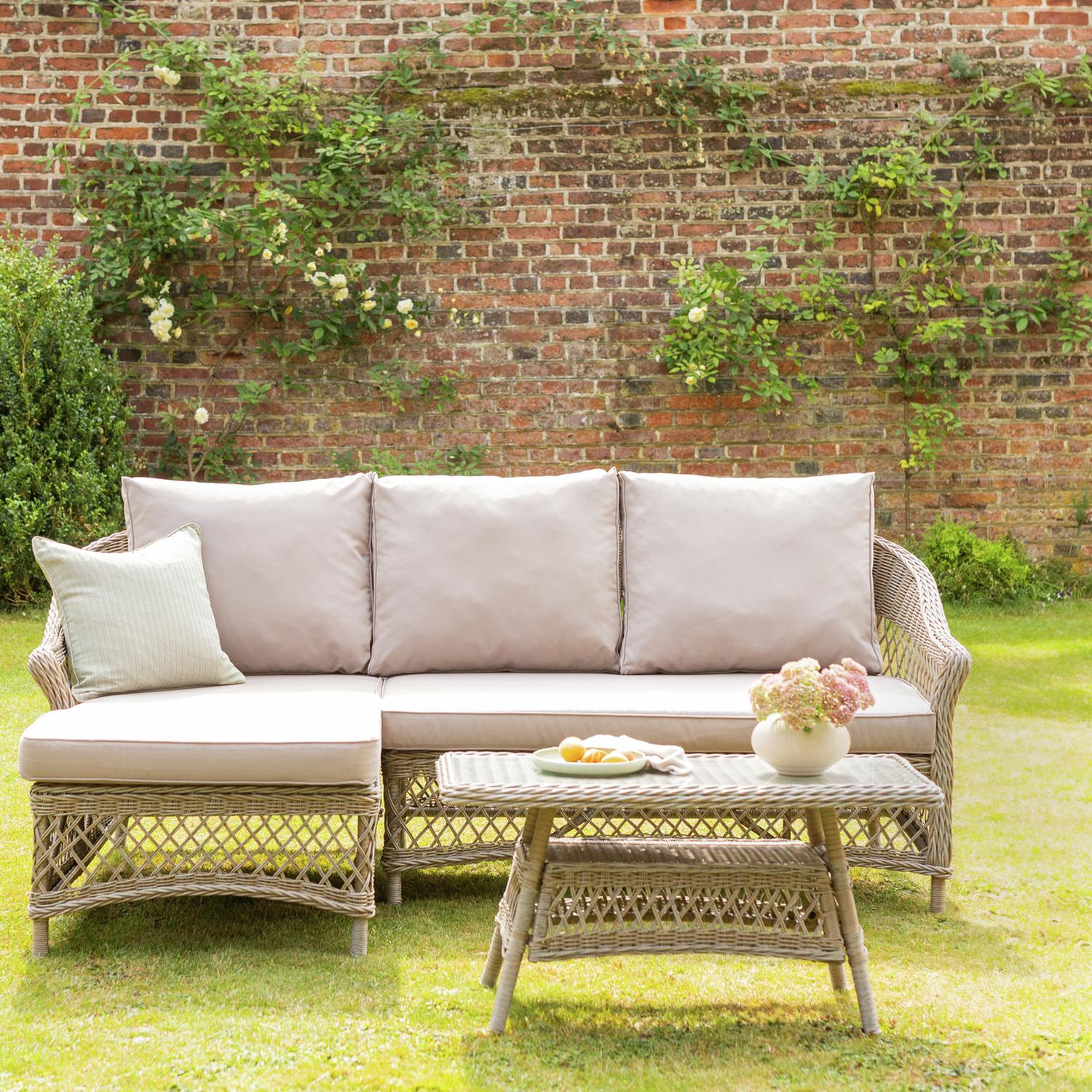 Luxury wicker garden sofa with beige cushions, matching table, and floral backdrop on lawn