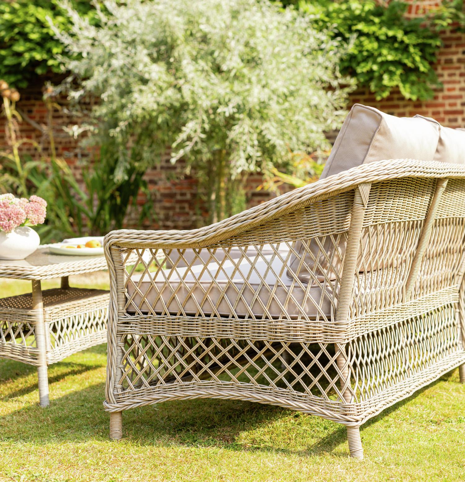Luxury wicker outdoor sofa with beige cushions on grass, perfect for garden relaxation and patio seating.