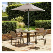 Outdoor patio set with glass table, wicker chairs, and large beige umbrella on stone terrace