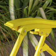 Bright yellow folding stool with textured seat, set against green foliage background