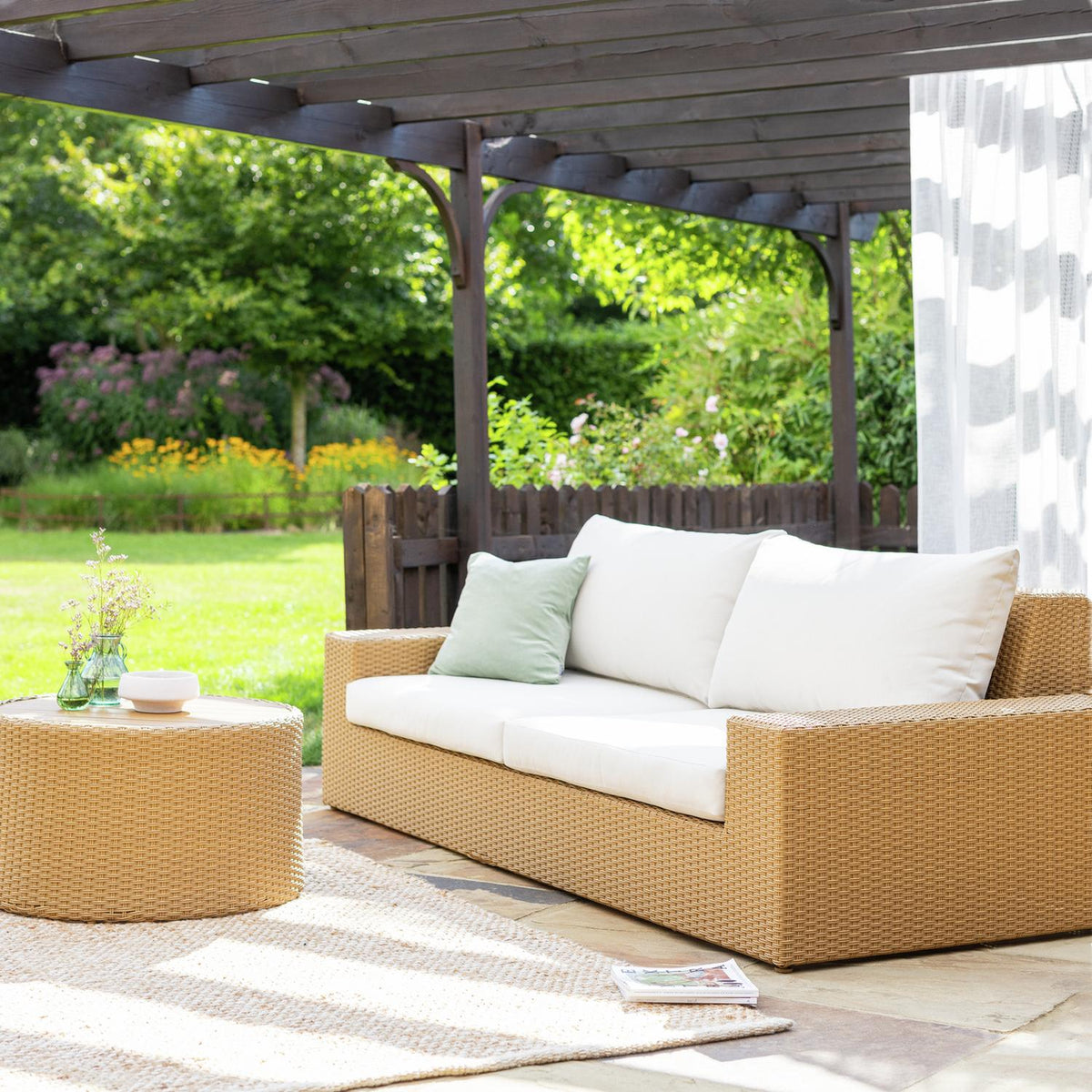Wicker outdoor sofa with white cushions under pergola in garden, perfect for luxury patio seating