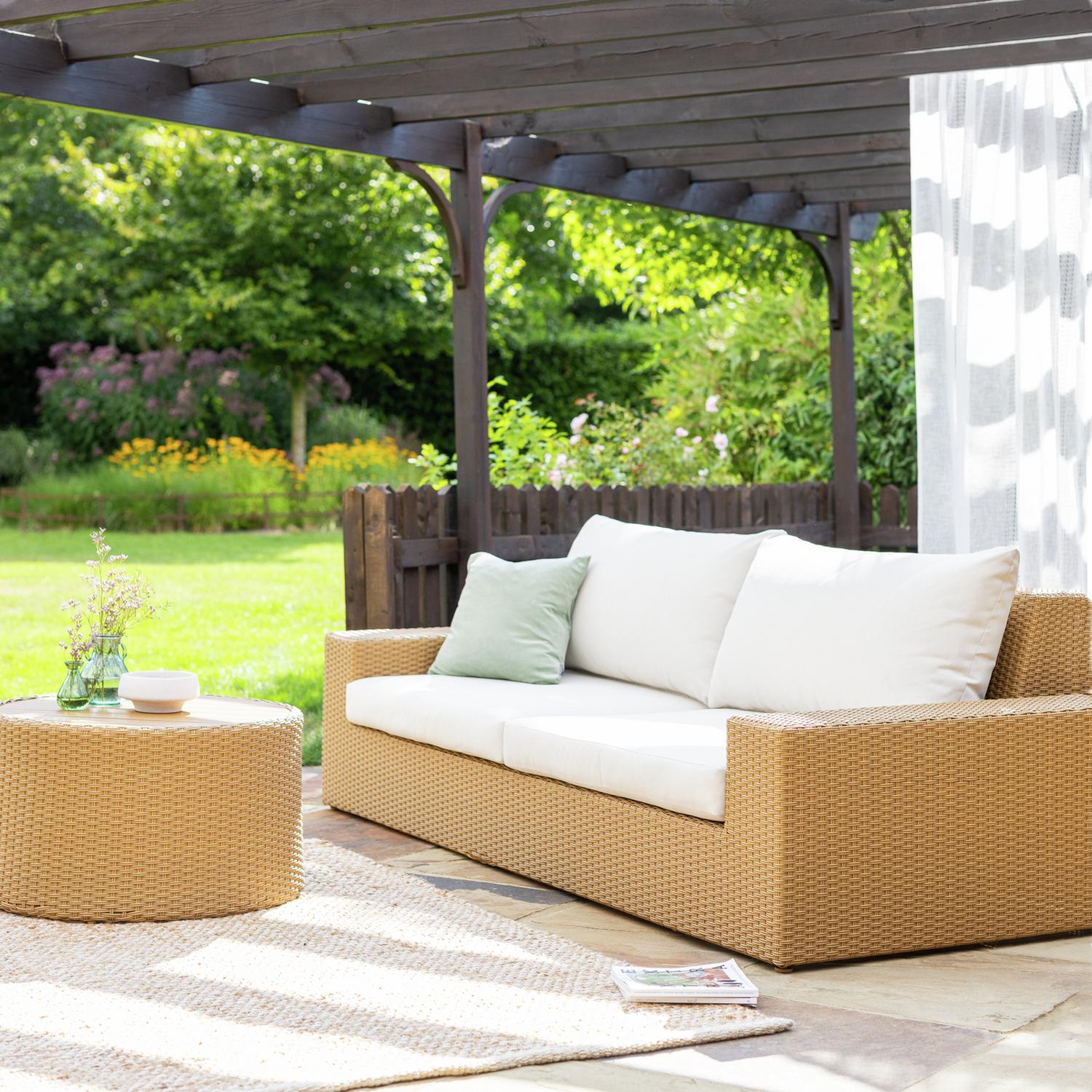 Wicker outdoor sofa with white cushions under pergola in garden, perfect for luxury patio seating