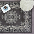 Grey vintage-style area rug with intricate floral pattern, styled with book, coffee cup, and knit pouf for cozy living room decor.