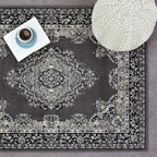 Grey vintage-style area rug with intricate floral pattern, styled with book, coffee cup, and knit pouf for cozy living room decor.