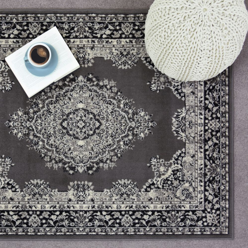 Grey vintage-style area rug with intricate floral pattern, styled with book, coffee cup, and knit pouf for cozy living room decor.