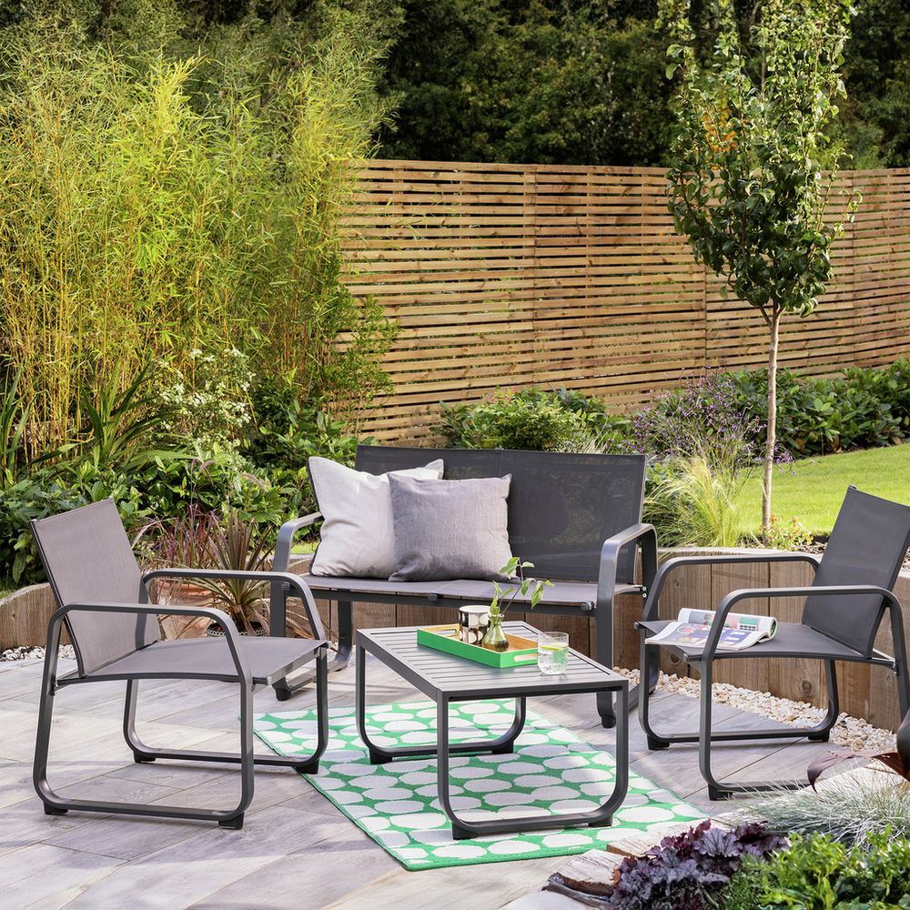 Modern outdoor patio furniture set with sofa, chairs, and coffee table on green rug in garden