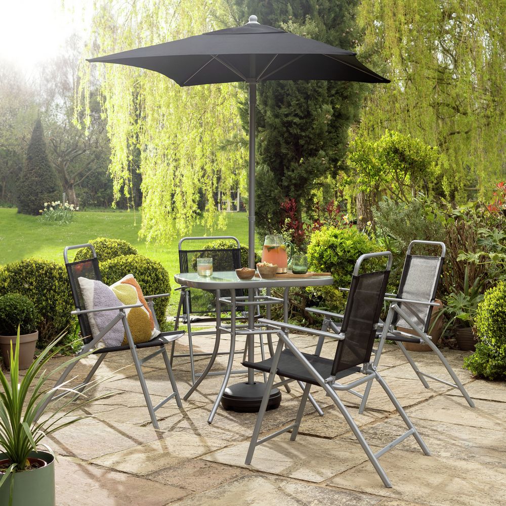 Outdoor patio set with glass table, 4 chairs, and black umbrella in lush garden