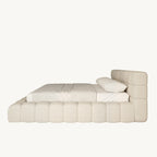 Modern upholstered bed with tufted headboard and base in cream fabric, side view