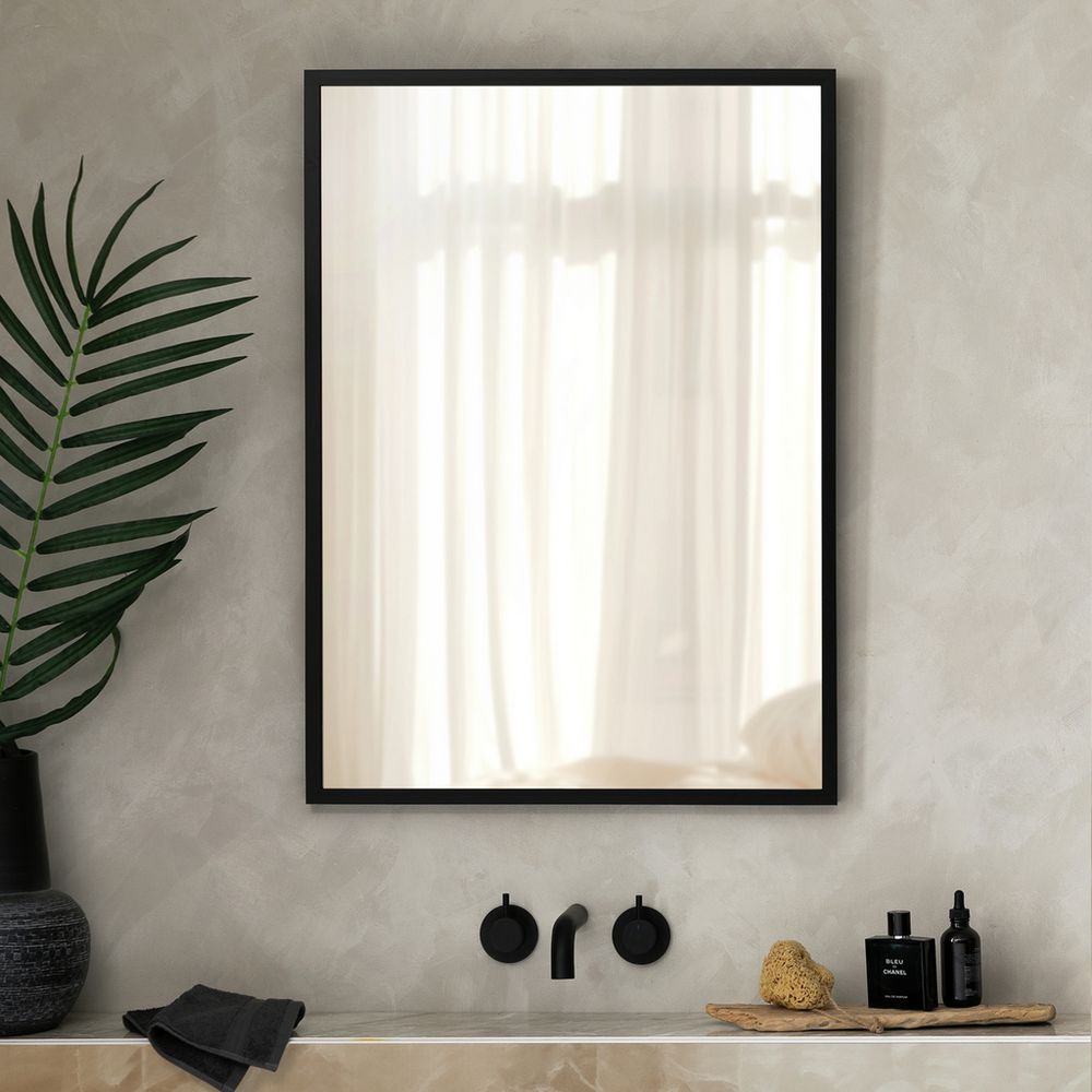Modern black-framed bathroom mirror with sleek fixtures, green plant, and luxury toiletries on marble vanity