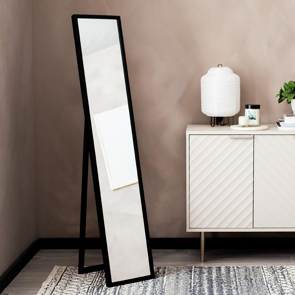 Black full-length floor mirror with A-frame stand in modern living room, beside white sideboard and lamp