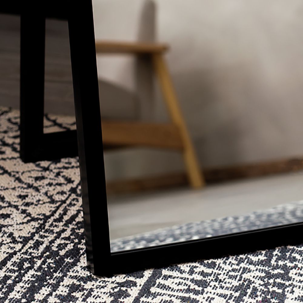 Black-framed mirror on patterned rug, reflecting wooden chair in modern living room