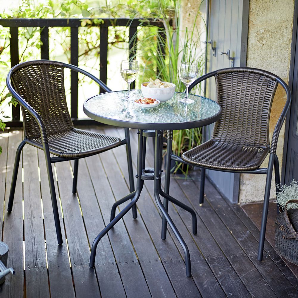 Outdoor wicker bistro set with glass table, two chairs, wine glasses, and snacks on wooden deck