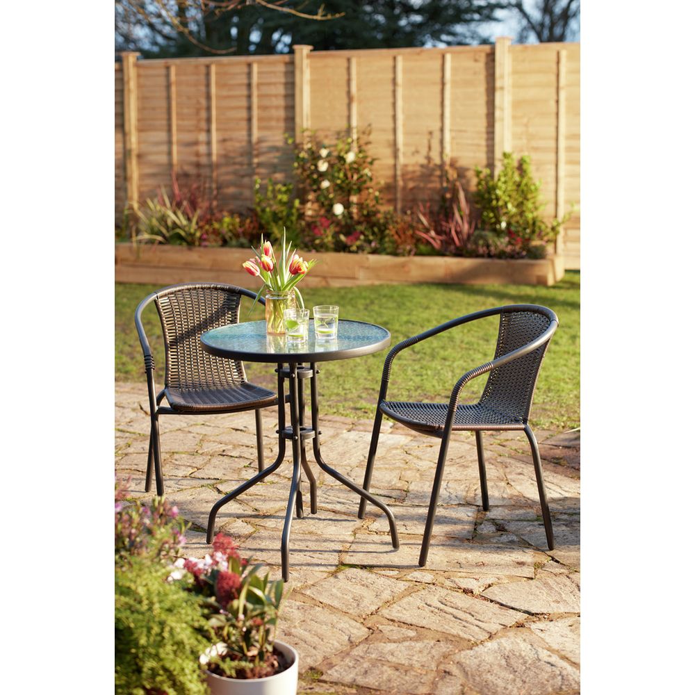 Outdoor bistro set with glass table and wicker chairs on stone patio, perfect for garden dining