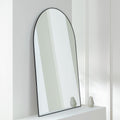 Arched black-framed wall mirror on white shelf with decorative vases, modern home decor