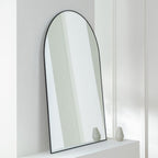 Arched black-framed wall mirror on white shelf with decorative vases, modern home decor