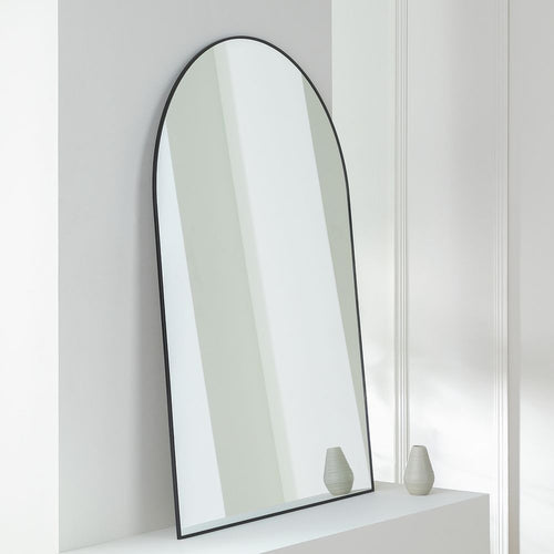Arched black-framed wall mirror on white shelf with decorative vases, modern home decor