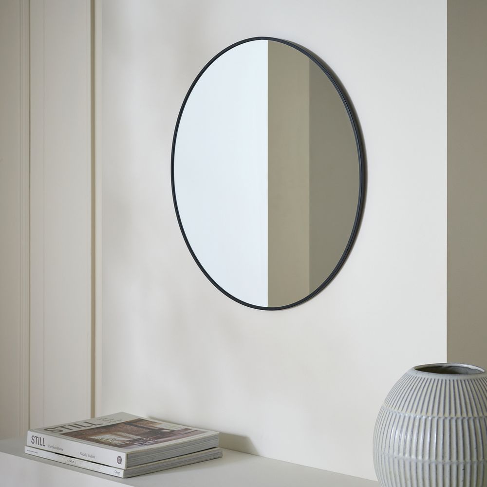 Round black-framed wall mirror in modern living space with books and vase
