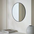 Round black-framed wall mirror in modern living space with books and vase