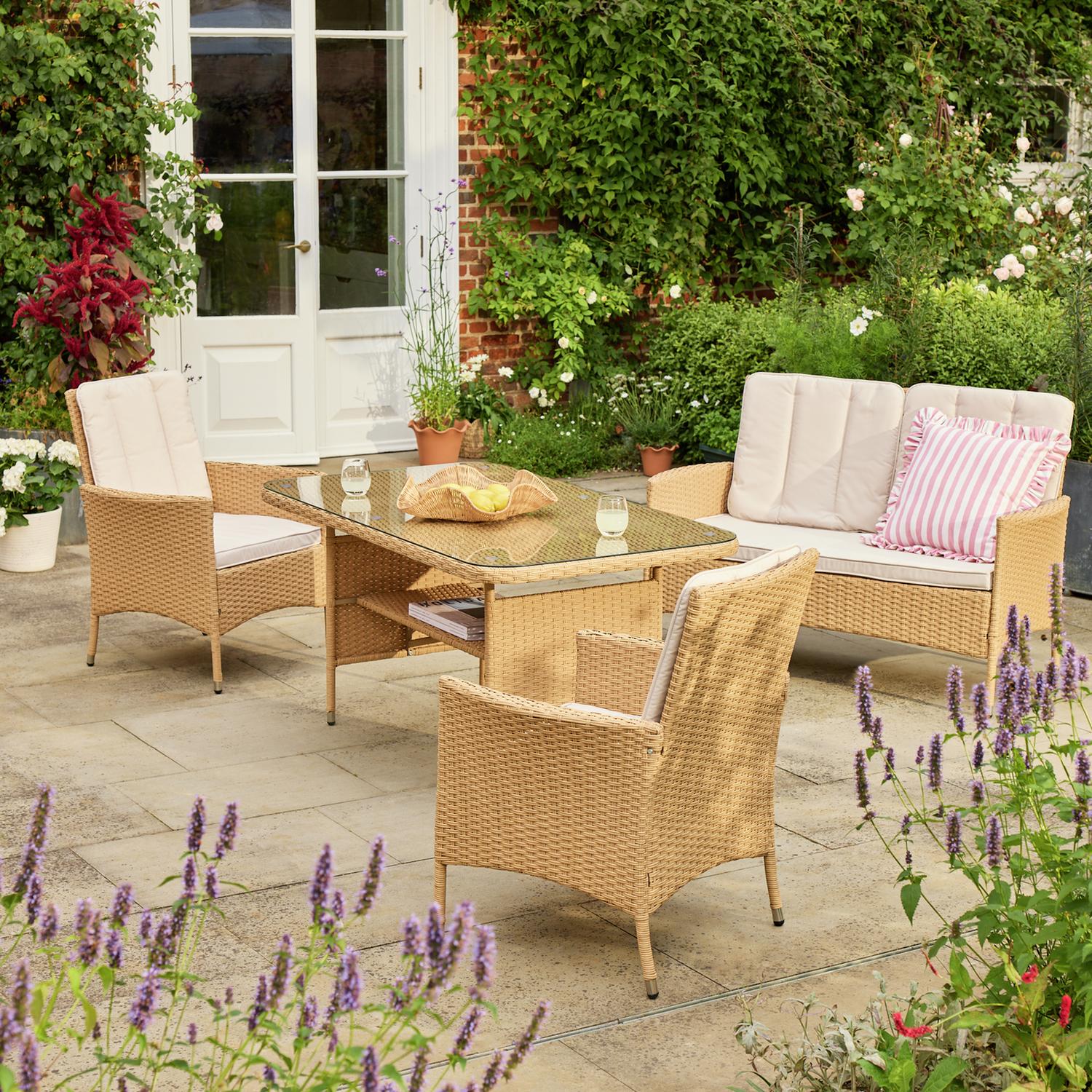 Rattan garden furniture set with glass table, cream cushions, and pink striped pillow on patio