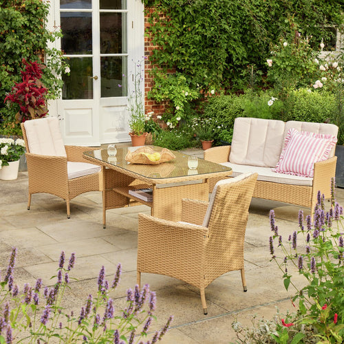 Rattan garden furniture set with glass table, cream cushions, and pink striped pillow on patio