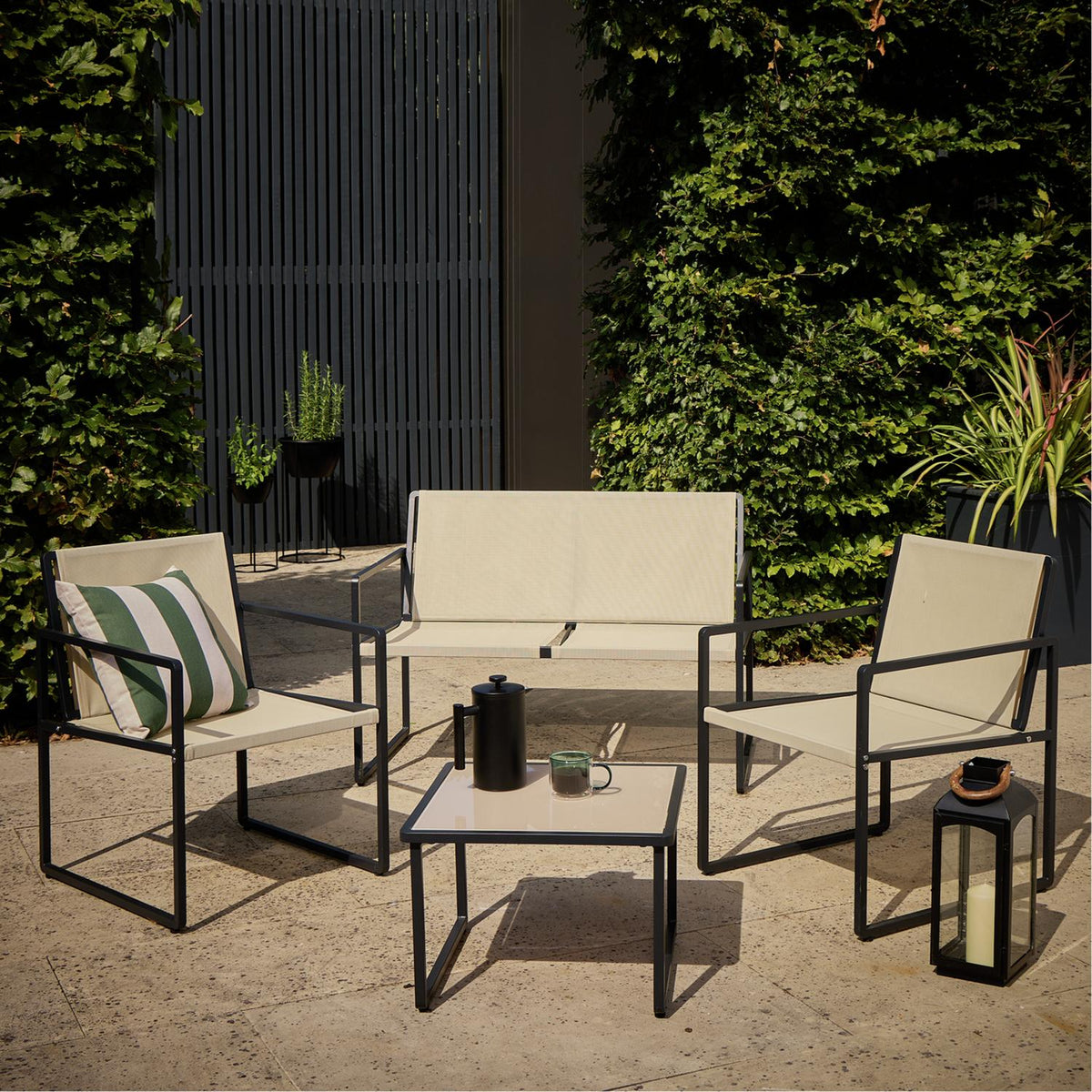 Modern outdoor patio set with beige fabric chairs, black metal frame, and glass-top table on stone terrace