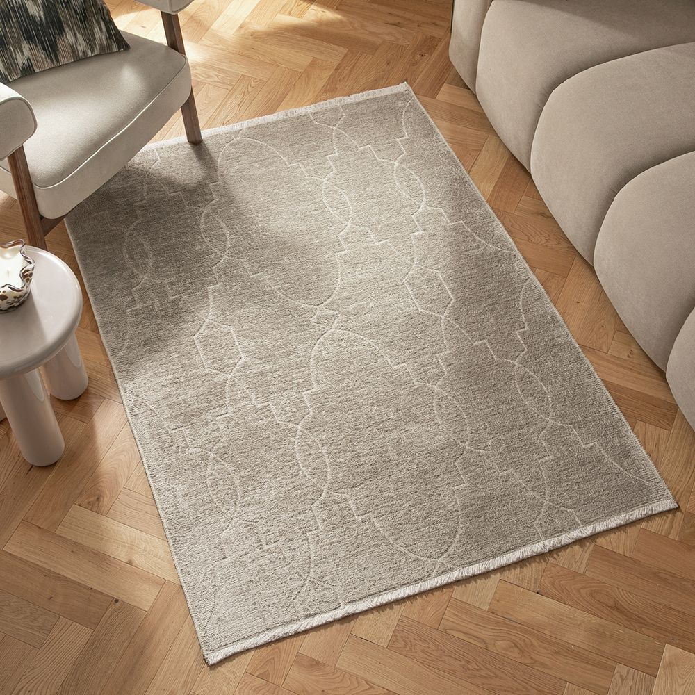 Beige geometric pattern rug on herringbone wood floor beside modern sofa and armchair