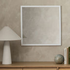 Modern white-framed wall mirror above wooden console with lamp and decor, luxury home styling
