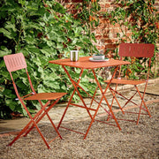 Rustic orange metal bistro set with two chairs and table in garden, perfect for outdoor dining or patio use.