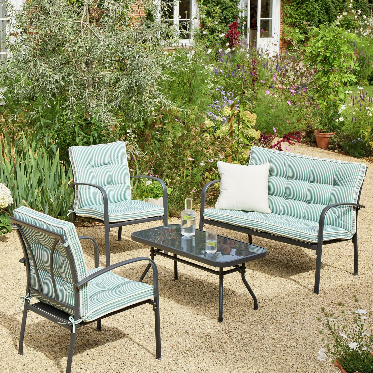 Striped outdoor garden furniture set with sofa, chairs, and glass table in lush backyard setting