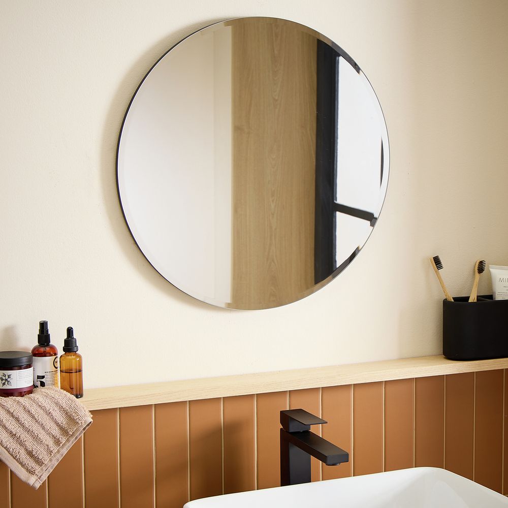 Round bathroom mirror with black frame above wooden vanity, modern sink faucet, and toiletries