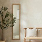 Tall wooden-framed mirror beside olive tree and woven bench in modern living room