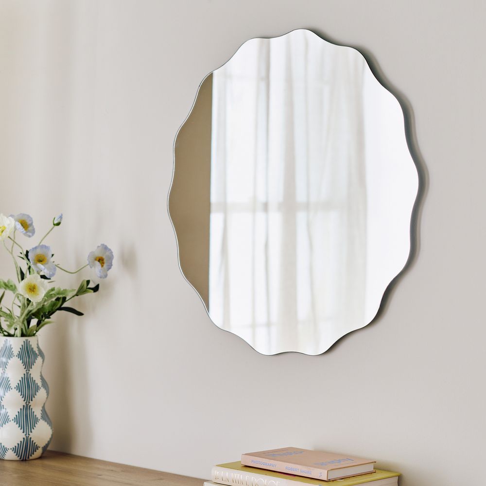 Scalloped edge wall mirror with floral vase and books, modern home decor