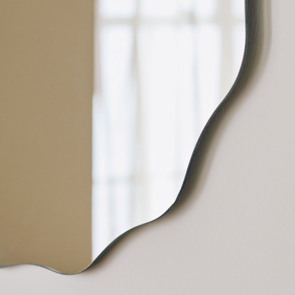 Modern wavy edge wall mirror with sleek black frame, reflecting soft natural light for contemporary home decor