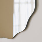 Modern wavy edge wall mirror with sleek black frame, reflecting soft natural light for contemporary home decor