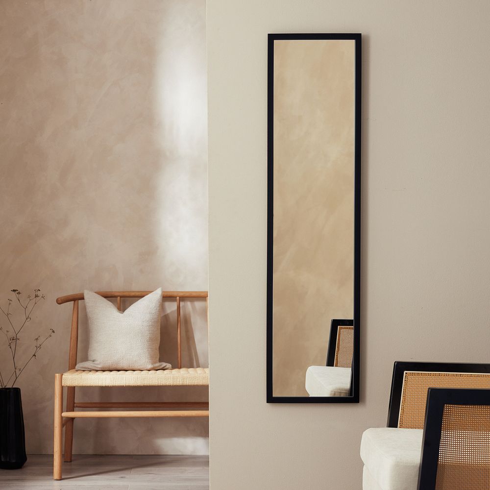 Tall black-framed wall mirror in modern living room with wooden bench and neutral decor