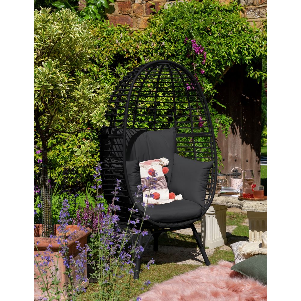 Black wicker egg chair with cushions in garden, perfect for luxury outdoor relaxation