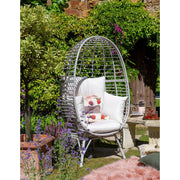 Grey wicker egg chair with white cushions in garden, perfect for luxury outdoor relaxation
