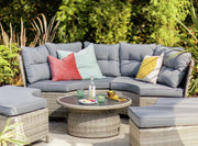 Grey wicker outdoor sofa set with colorful cushions, round table, and garden backdrop